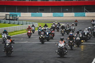 A group of motorcyclists riding closely on a smooth race track under clear skies.