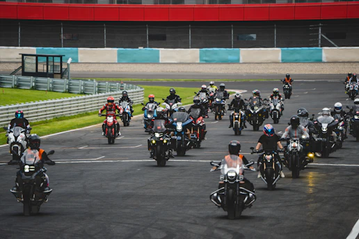 A group of motorcyclists riding closely on a smooth race track under clear skies.