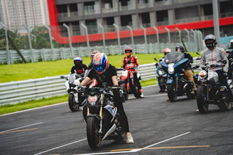 A group of riders geared up in bold red and black apparel preparing for a race in the shadow of grandstands.