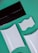 A flat lay composition of various packaging and design elements displayed on a green background. There is a black rectangular envelope, two white rectangular boxes with curved surfaces, and a white piece with wavy ridges. The items are positioned at diagonals, creating a dynamic layout.