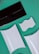A flat lay composition of various packaging and design elements displayed on a green background. There is a black rectangular envelope, two white rectangular boxes with curved surfaces, and a white piece with wavy ridges. The items are positioned at diagonals, creating a dynamic layout.