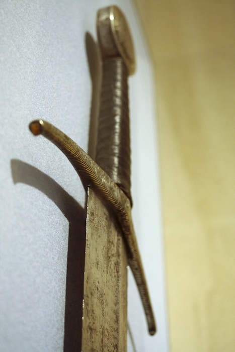 A medieval sword with a long, slightly corroded blade and a hilt wrapped in textured material. The cross-guard is simple and slightly curved. The pommel appears round and heavy, indicative of swords from the Middle Ages.
