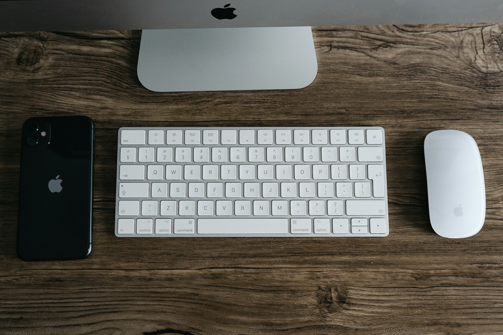 a keyboard, mouse, and iphone on a wooden table