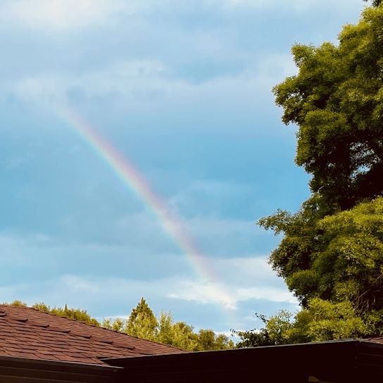 A bright, colorful double rainbow arching over the Autistry Studios building on a sunny day.
