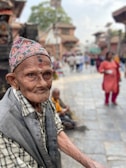 An elderly man in India, his weathered face telling tales of resilience, framed against a vibrant market backdrop.