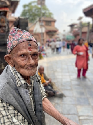 An elderly man in India, his weathered face telling tales of resilience, framed against a vibrant market backdrop.