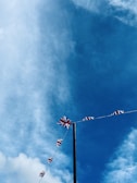 A string of Union Jack flags is strung across a tall pole against a backdrop of a vivid blue sky with scattered clouds.