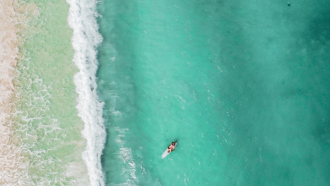 a person riding a surf board on a body of water, Drone picture with surfer laying on a surfboard.