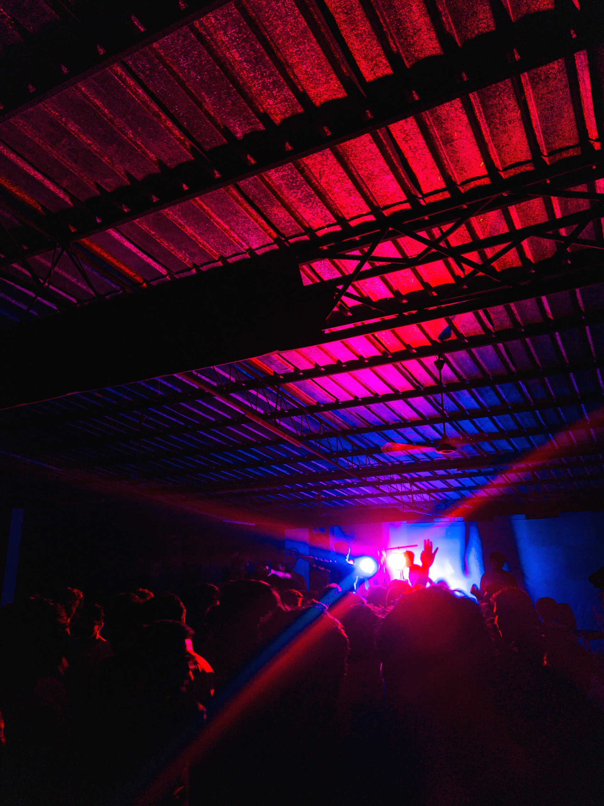 A wide view of the main room showcasing the brutalist minimalism, red accents, and a live event with guests immersed in music.