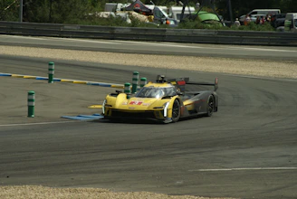 A powerful race car speeding through a sharp curve under bright yellow and black banners, capturing the thrill of motorsport.