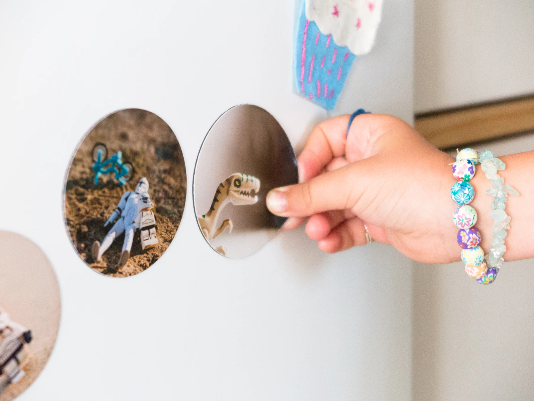 A hand pressing a round photo magnet onto a white fridge door, next to another round photo magnet