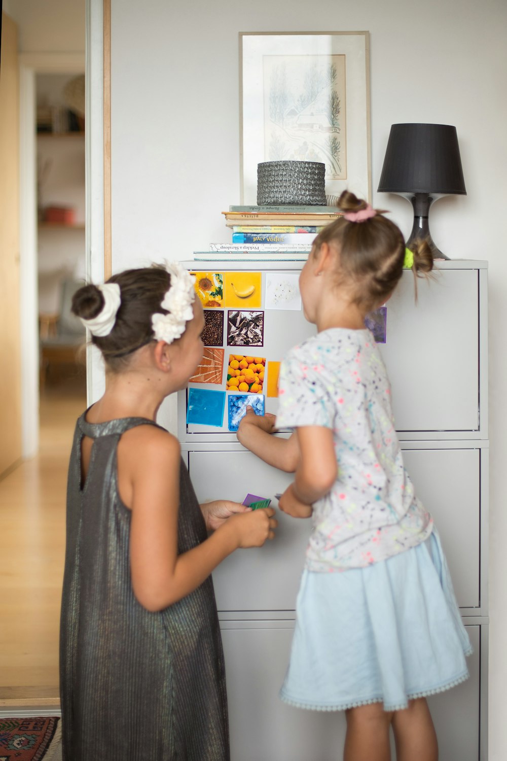 two little girls standing next to each other in front of a filing cabinet