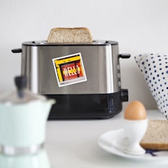A modern toaster with golden-brown toast popping up, set on a bright kitchen countertop.