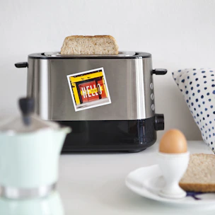 A compact toaster with golden-brown toast popping up, set against a bright kitchen backdrop.