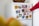 A hand with a red sleeve is touching the door of a white refrigerator covered with colorful pictures of various fruits such as oranges, pears, blueberries, pomegranates, and kiwis. On top of the refrigerator is a woven basket.