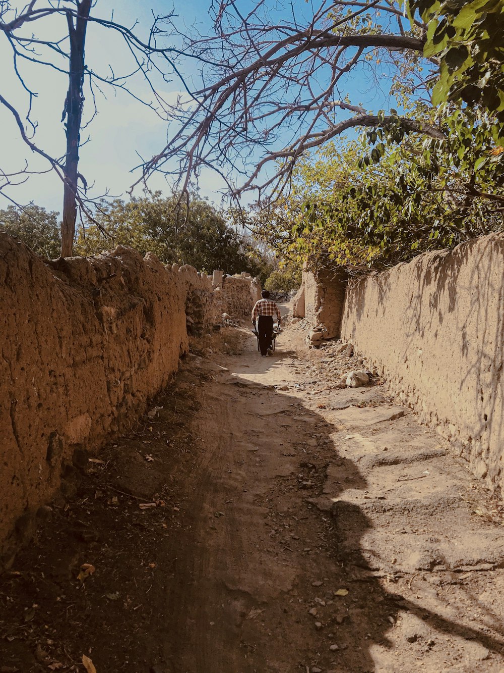 a person walking down a dirt road next to a stone wall