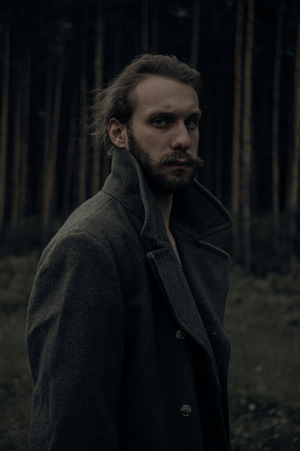 a man with a beard standing in front of a forest