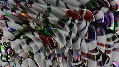 An abstract digital artwork featuring a complex pattern of swirling forms and shapes. The image is composed of intertwining colors that include shades of red, green, blue, and black, creating a sense of depth and movement. The textures appear smooth and reflective, suggesting a glossy or metallic surface.