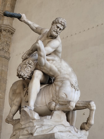 A classical marble sculpture depicting a muscular figure engaged in a dynamic struggle with a centaur. The composition is intense, with the human figure gripping the centaur firmly, showcasing a dramatic and energetic pose.