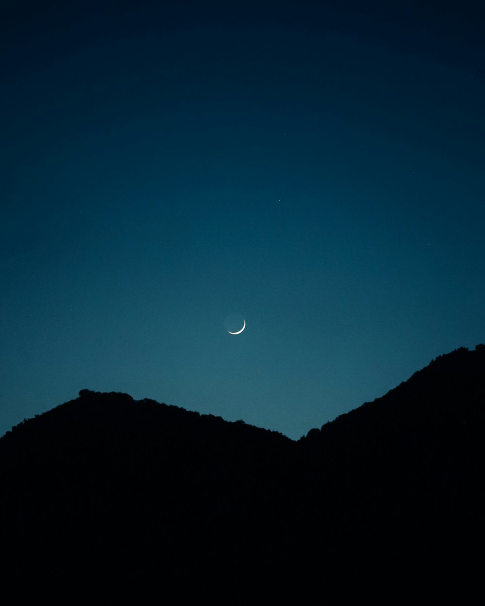 the moon is seen in the sky above a mountain