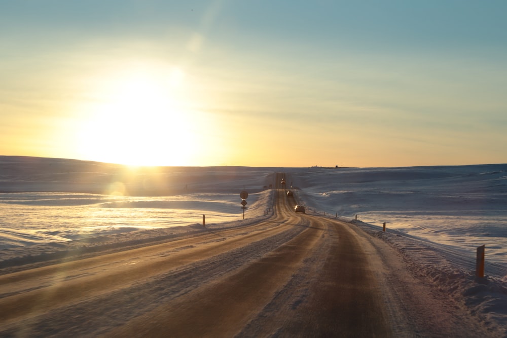 the sun is setting over a snowy road