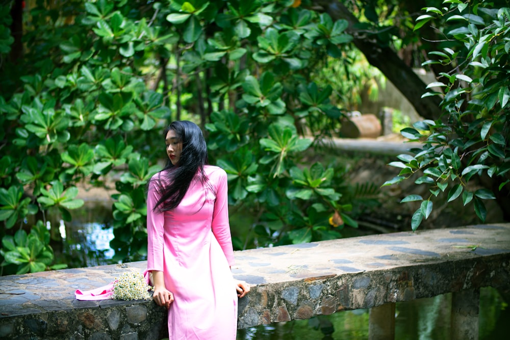 a woman in a pink dress standing on a stone wall