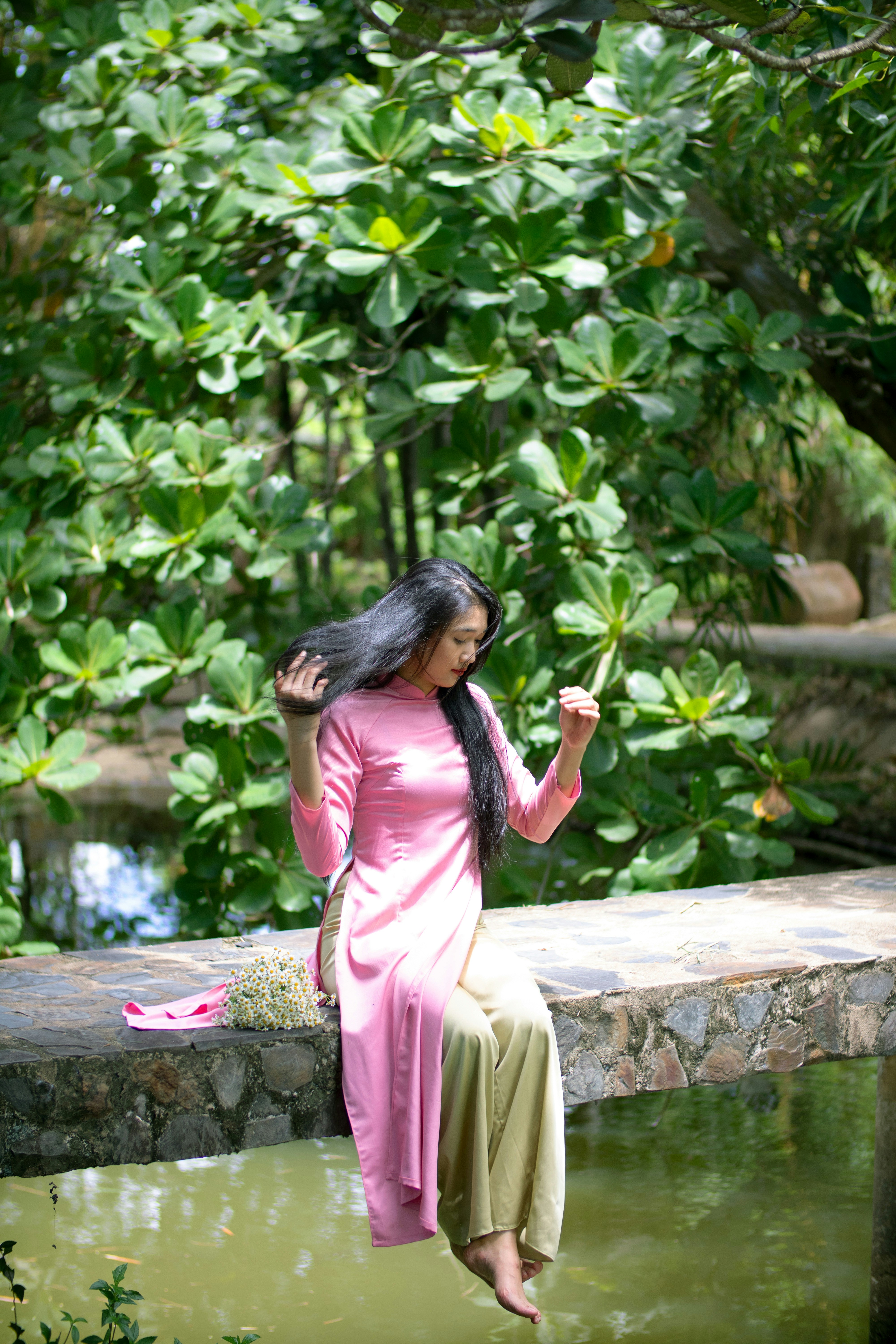a woman in a pink dress sitting on a stone wall