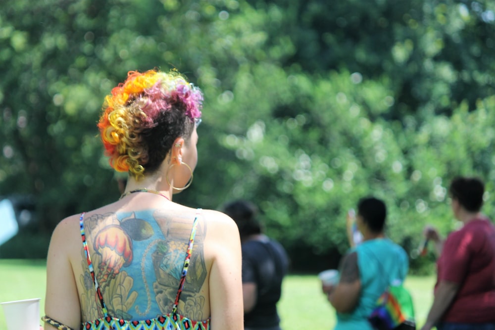 a woman with tattoos on her back standing in a park