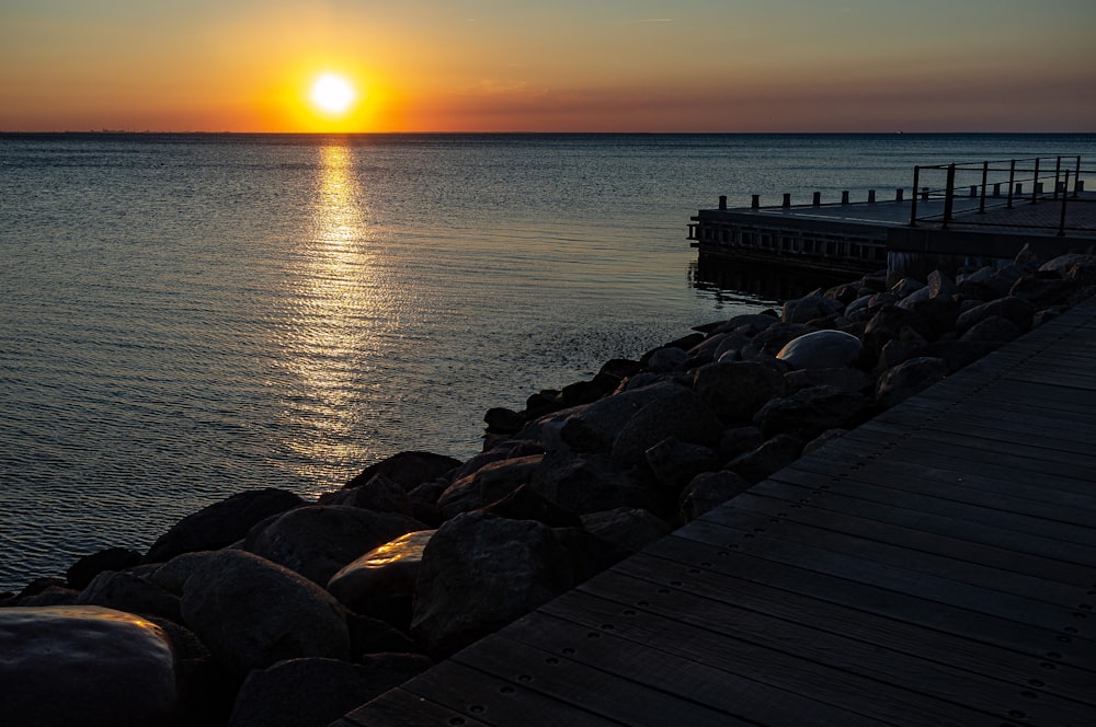 the sun is setting over the water at a pier