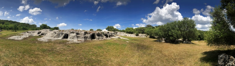 A panoramic view of the three Cuesta stones surrounded by cerrado vegetation under a clear sky.