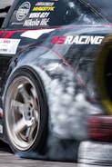 A close-up shot of a drifting car's tire smoke curling around the rear wheel.