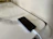 A smartphone is placed on a marble surface. The phone is connected to a magnetic charging cable. The surface has a smooth, reflective finish with subtle gray veining.