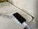 A smartphone is placed on a marble surface. The phone is connected to a magnetic charging cable. The surface has a smooth, reflective finish with subtle gray veining.