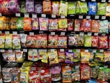 A supermarket shelf filled with various colorful packaged candies and snacks. The assortment includes well-known brands like Skittles, Haribo gummies, mints, and other assorted sweets neatly arranged. Each product has a visible price label, and the packaging features vibrant colors and eye-catching designs.
