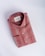 A neatly folded, striped shirt in shades of red and beige, featuring a tag with branding inside the collar. The shirt has a classic design, including buttons and a pocket detail on a smooth, neutral background.