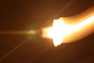 A bright, glowing light source with a yellow and orange gradient appears to be moving in a curved path against a dark background, creating a sense of motion and energy.