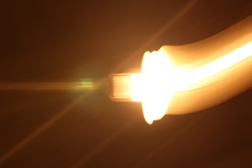 A bright, glowing light source with a yellow and orange gradient appears to be moving in a curved path against a dark background, creating a sense of motion and energy.