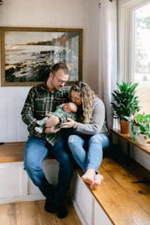 a man and woman sitting on a window sill holding a baby