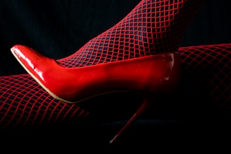 a woman's red high heeled shoe with fishnet stockings