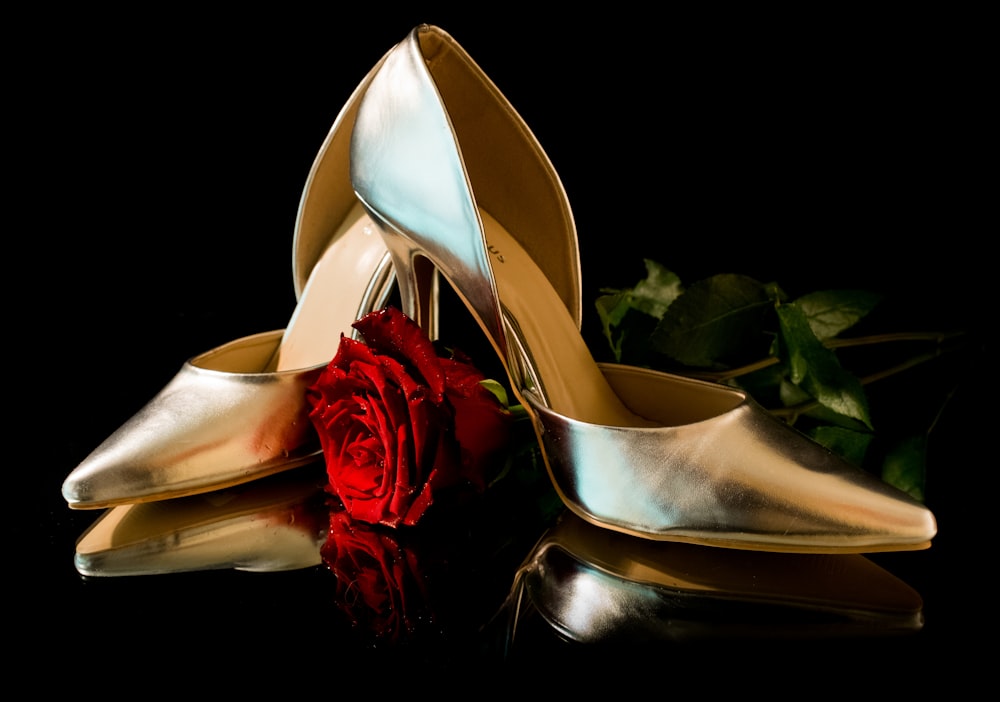 a pair of gold high heel shoes next to a red rose