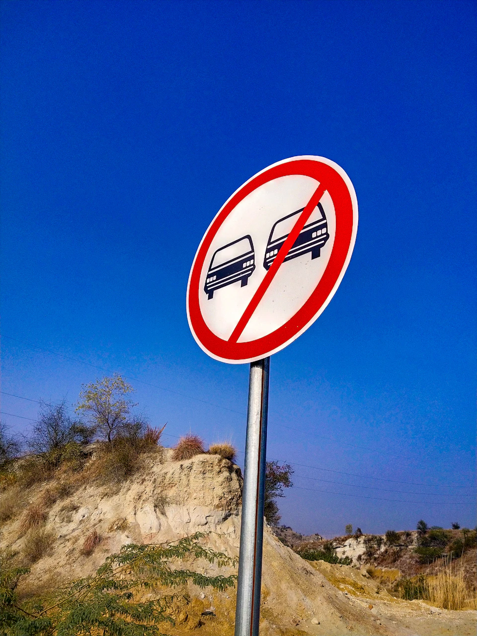 Red circular traffic sign mounted on metal pole stands against clear blue sky with cars