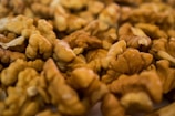 A close-up view of a pile of unshelled walnuts, showcasing their intricate, curved shapes and textures. The nuts display a natural brown color, and the scene is warmly lit, highlighting the intricate details of the walnut surfaces.