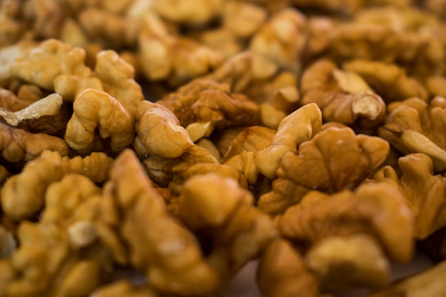 A close-up view of a pile of unshelled walnuts, showcasing their intricate, curved shapes and textures. The nuts display a natural brown color, and the scene is warmly lit, highlighting the intricate details of the walnut surfaces.