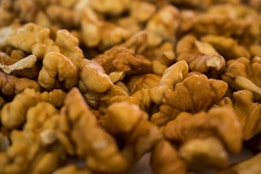 A close-up view of a pile of unshelled walnuts, showcasing their intricate, curved shapes and textures. The nuts display a natural brown color, and the scene is warmly lit, highlighting the intricate details of the walnut surfaces.
