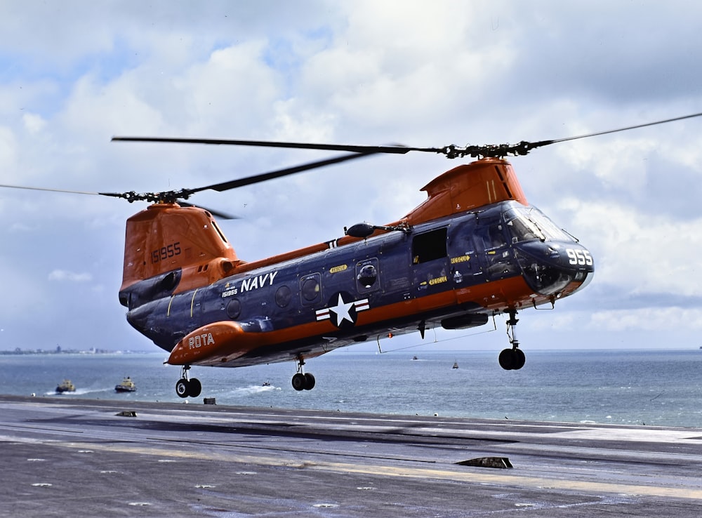 a blue and orange helicopter taking off from an aircraft carrier