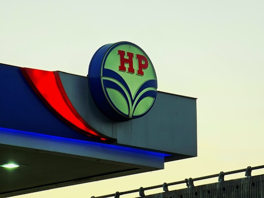An outdoor sign displaying the HP logo in red letters on a circular background with green elements. The sign is part of a larger structure with blue and red accent lighting, set against a light sky backdrop.