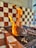 A piece of meat is being grilled with visible flames rising from the grill. The background features a checkered pattern of red and white tiles, indicative of a barbecue setting.