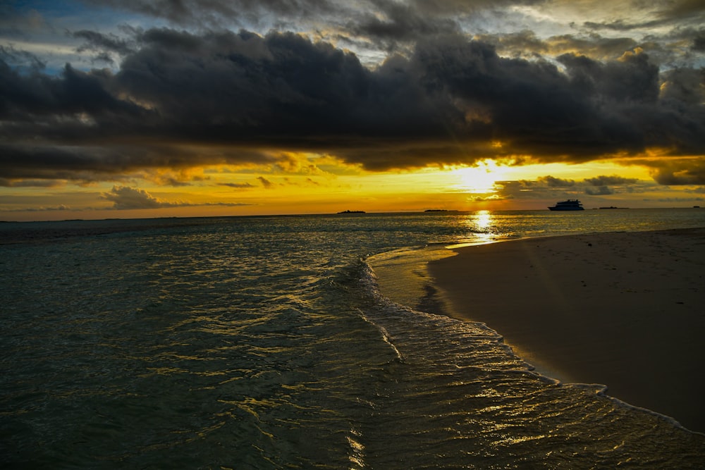 the sun is setting over the ocean with a boat in the distance