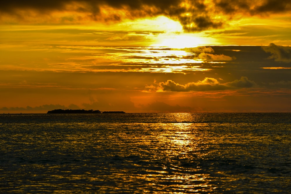 the sun is setting over the ocean with a small island in the distance