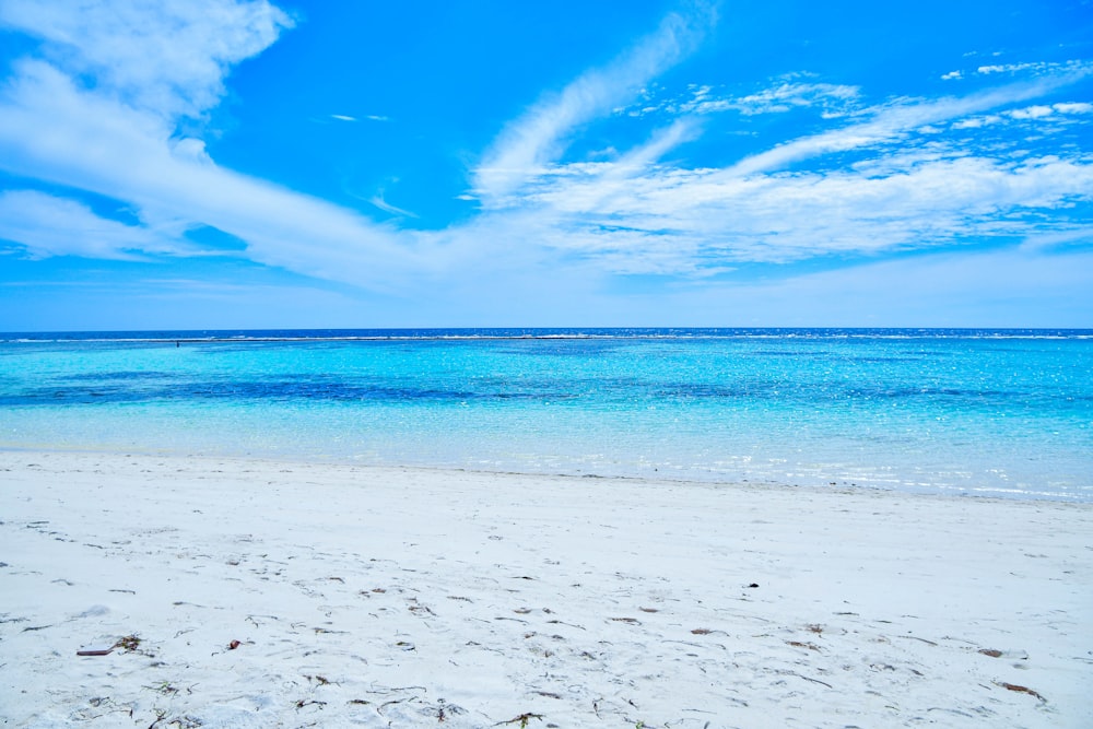 a white sandy beach with blue water and clouds